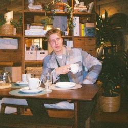 Portrait of Jesse sitting behind a dinner table with a coffee cup in hand